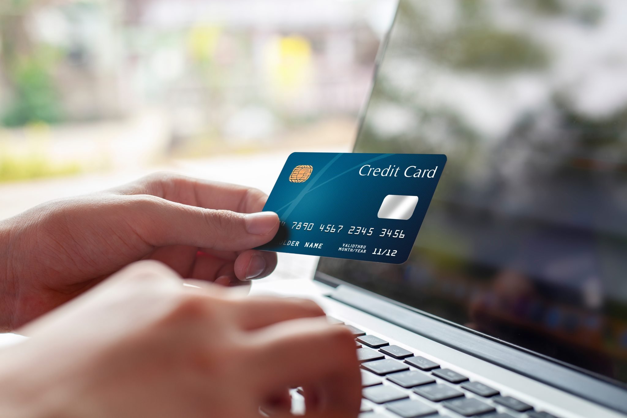 Woman hand holding blue credit card and using modern laptop