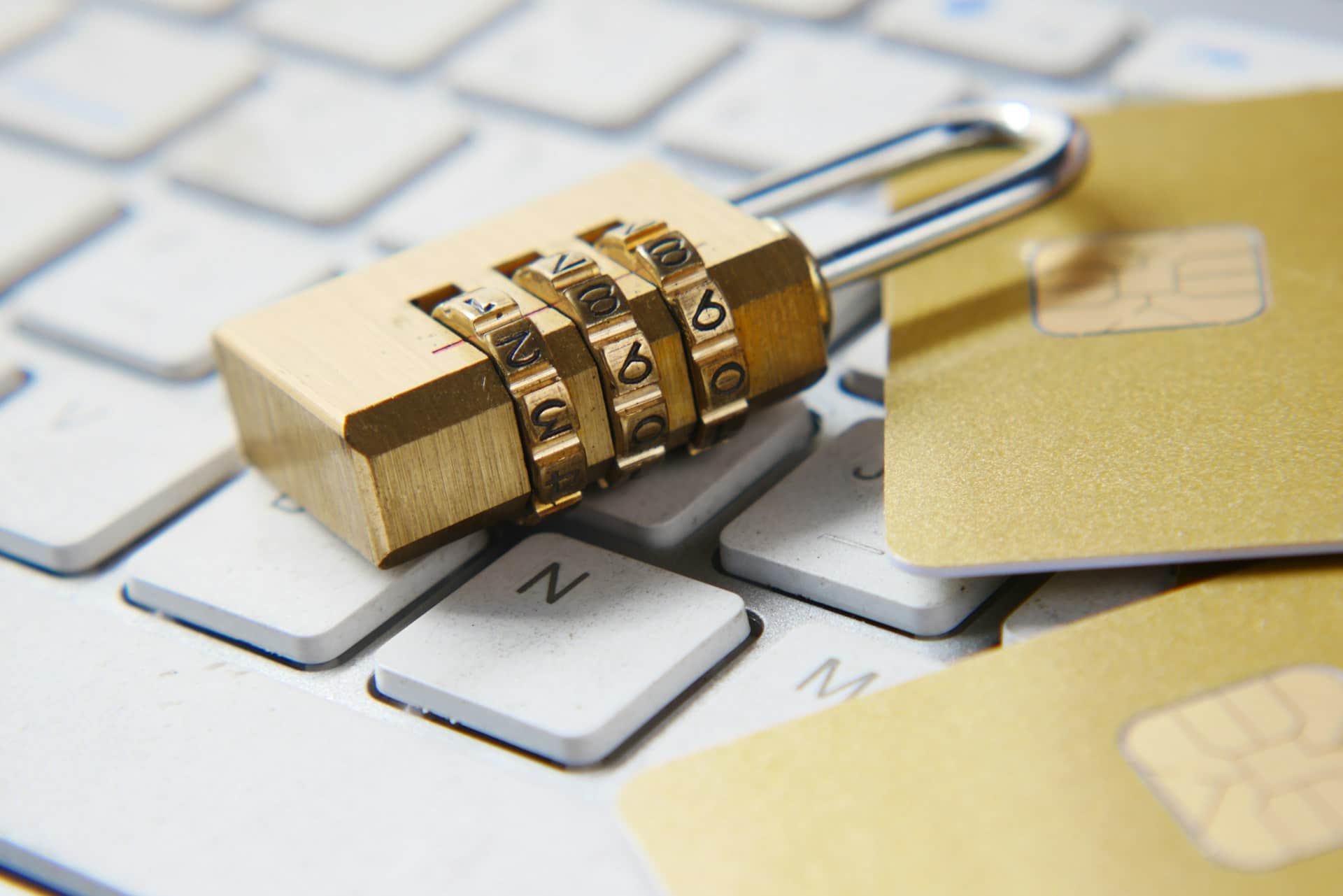 A golden padlock sitting on a keyboard next to credit cards